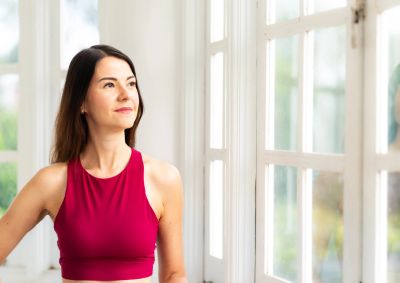 Woman in red athletic top looking outside thoughtfully.
