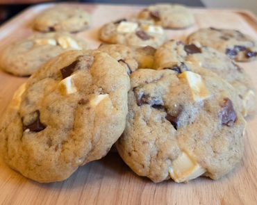 Freshly baked cookies with white and dark chocolate chunks on a wooden surface.