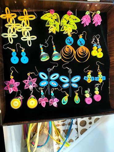 Colorful handmade quilled paper earrings arranged on black fabric.
