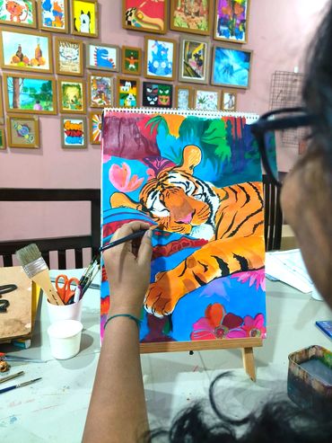 Artist painting a vibrant tiger portrait in a colorful studio filled with framed artwork.