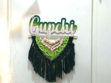 Decorative wall hanging with the word 'Gupchi' and colorful fabric tassels.