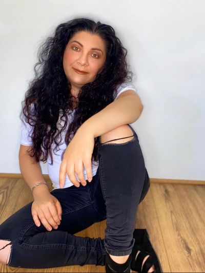 Woman with long curly hair sits on wooden floor against plain wall.
