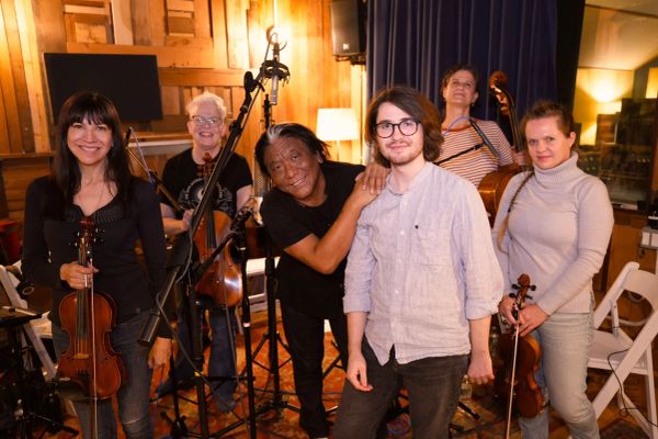 Group of musicians posing with string instruments in a cozy room.