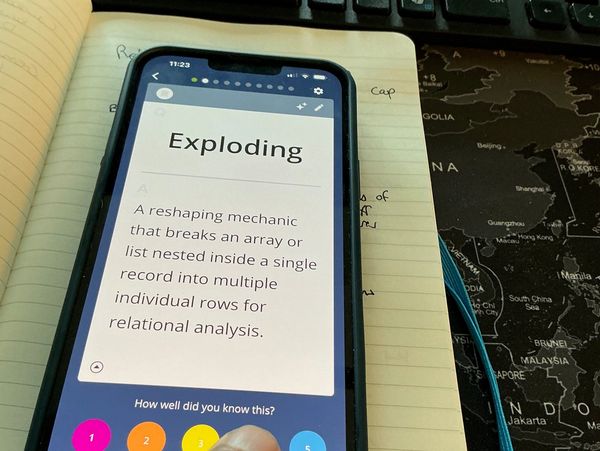 Phone displaying definition of 'Exploding' with a notebook and map background.