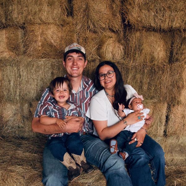A happy family of four sitting on hay bales in a rustic setting.