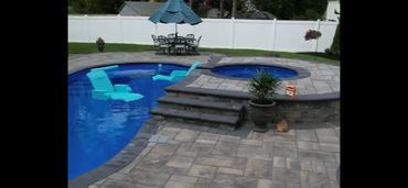 Backyard pool with blue lounge chairs and a hot tub under a blue umbrella.