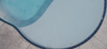 Top-down view of a small backyard pool with concrete surroundings and a stone border.