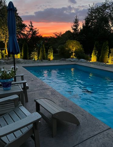 Backyard pool at sunset with illuminated trees and patio furniture.