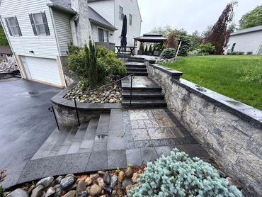 Wet stone steps and patio leading to a house with a garden and gazebo.