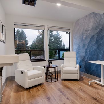an iv room with two white leather chairs and a table in the middle to administer iv fluid.