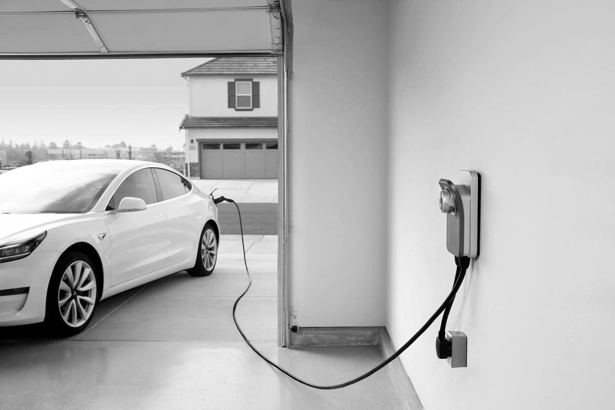 White electric car charging in a garage with a wall-mounted charger.
