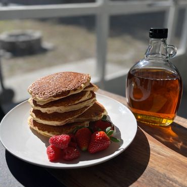 Stack of pancakes with strawberries and syrup on a wooden table.