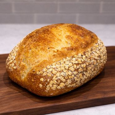 A loaf of oat-crusted bread on a wooden cutting board.