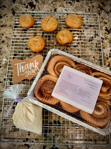 Freshly baked sourdough cinnamon rolls and cookies with a thank you note on a cooling rack.
