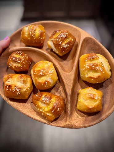 Freshly baked pretzel bites sprinkled with coarse salt on a wooden divided plate.