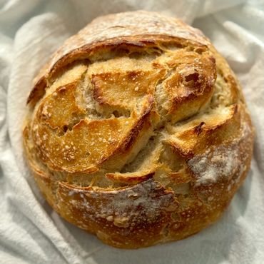 A freshly baked round loaf of crusty artisan bread on a white cloth.