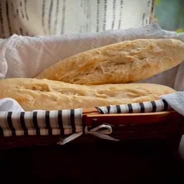 Two baguettes in a basket lined with white and striped cloth.