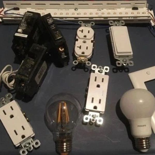 Various electrical components including switches, outlets, breakers, and light bulbs on a dark surface.
