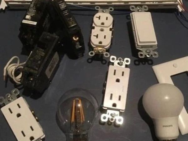 Various electrical components including outlets, switches, and light bulbs on a dark surface.