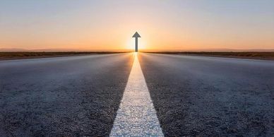 Road leading to sunrise with an arrow.