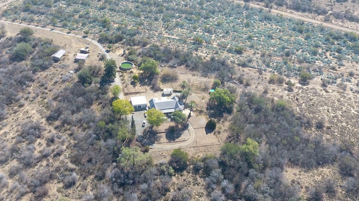 A farmstead surrounded by trees and farmland in a dry landscape.