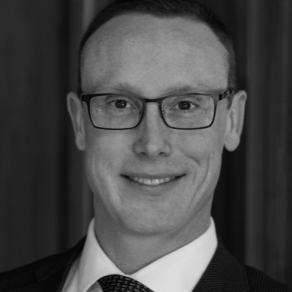 Black and white headshot of a smiling man wearing glasses and a suit.