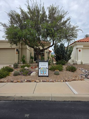 Residential front yard with desert landscaping and a tree service sign.