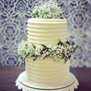 A  two tiered rustic white wedding cake with white baby's breath flowers surround the cakes.