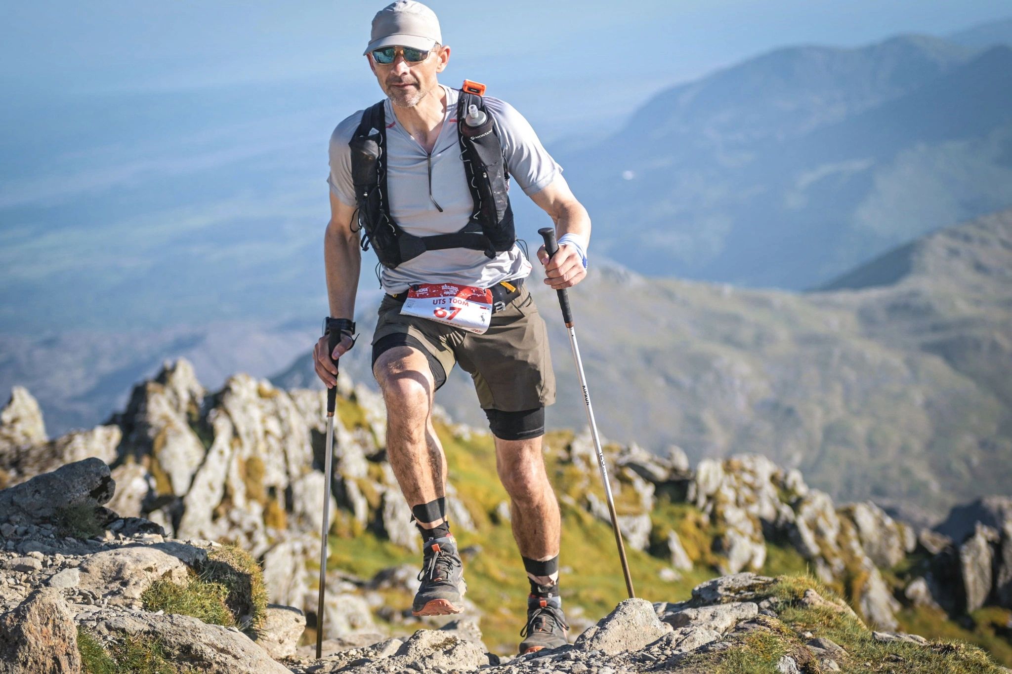 Trail runner in a mountain setting looking determined to push on, using poles