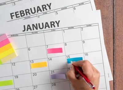 Hand marking dates on January calendar with colorful sticky notes nearby.