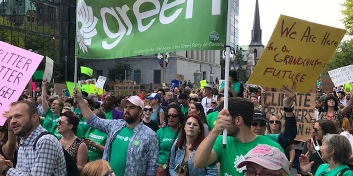 A large crowd at a climate change protest holding signs and a Green Party banner.