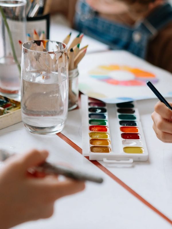Watercolor paints and pencils on a table with people painting.