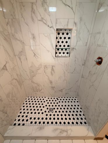 Shower with marble wall tiles and black-and-white patterned floor tiles.