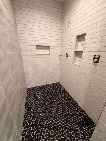 Modern shower with white subway tiles and black hexagonal floor tiles.