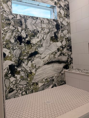 Modern shower with striking black, white, and green marble wall and hexagonal tile floor.