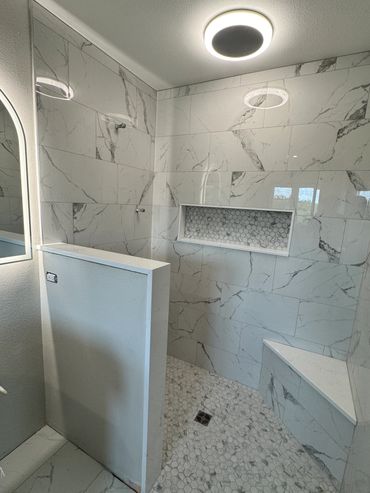 Modern bathroom shower with marble tiles and built-in bench.