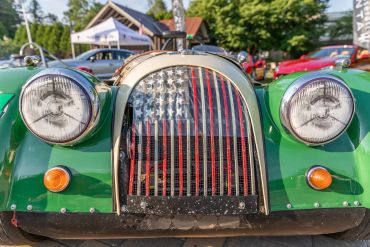 Front view of a green vintage car with an American flag grille.