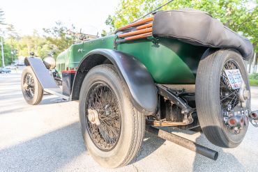 Close-up of a vintage green car's rear with spare tires and wooden details.