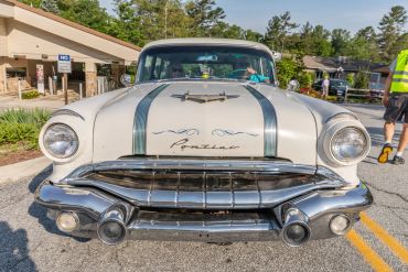 Front view of a vintage white Pontiac car with people inside.