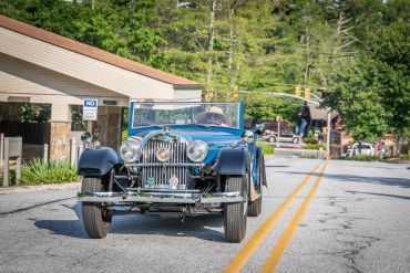 A person driving a vintage blue car on a sunny day.