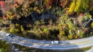 Aerial view of a winding road with cars and colorful autumn foliage.