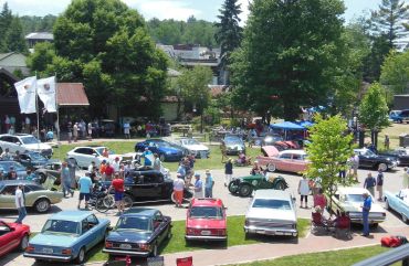 Vintage and modern car show with people outdoors on a sunny day.