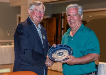 Two men smiling and holding a blue ceramic plate together.