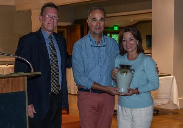 Three adults posing indoors, one holding a ceramic vase.