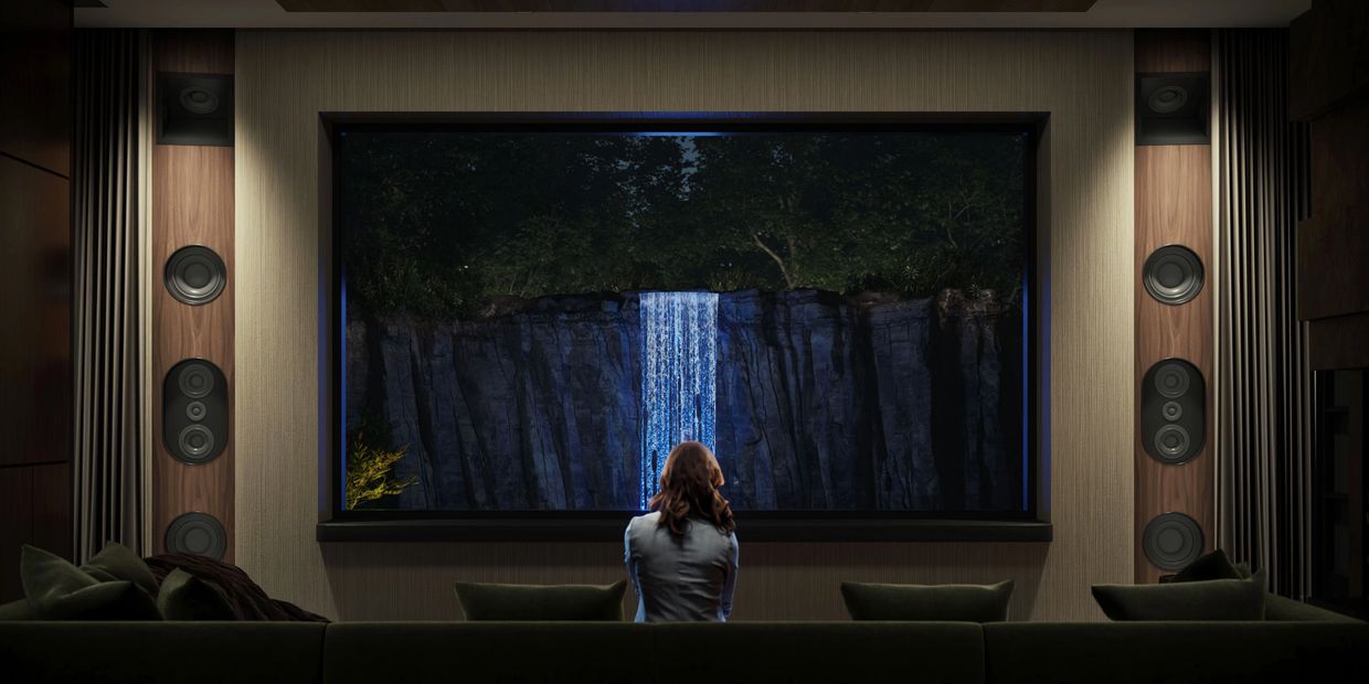Person watches illuminated waterfall through large window in cozy room.