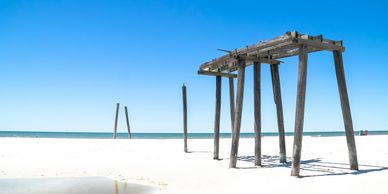 Old wooden pier remains on a bright, sunny beach with clear blue skies.