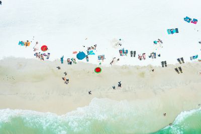 Aerial view of beachgoers relaxing on white sand near turquoise water.