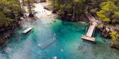 A clear blue natural spring with people swimming and a wooden dock.