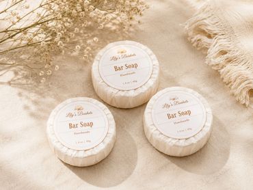 Three handmade bar soaps from Lily's Baskets on a beige fabric.