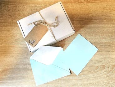 Gift box tied with twine and a blank tag, with an open blue envelope on a wooden surface.